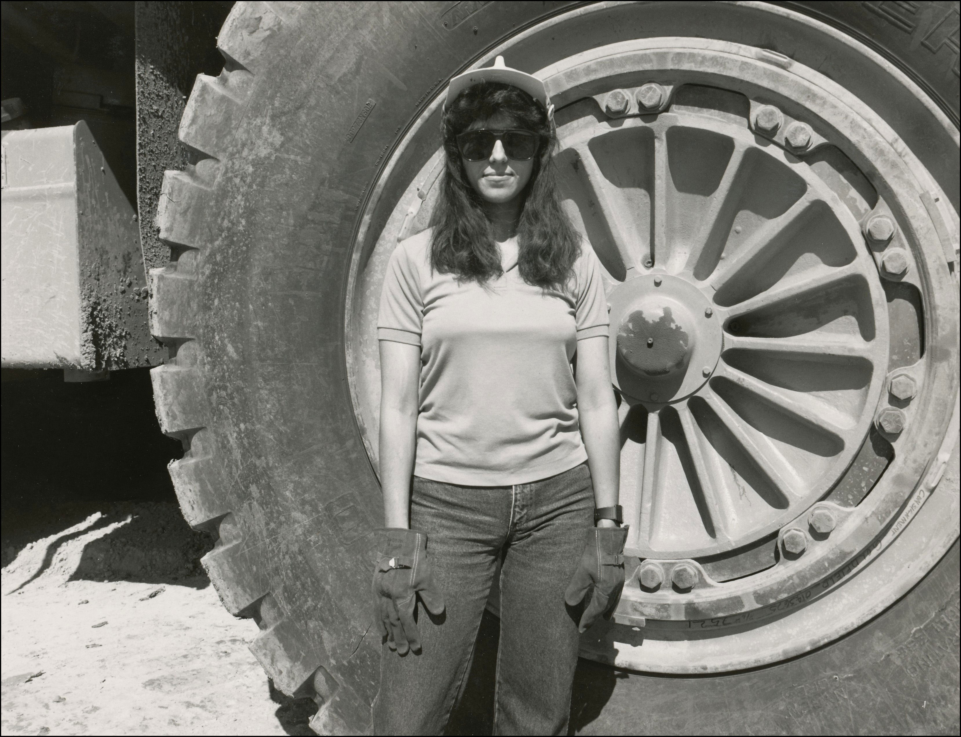 Miner woman standing in front of a very large tire on a piece of construction equipment