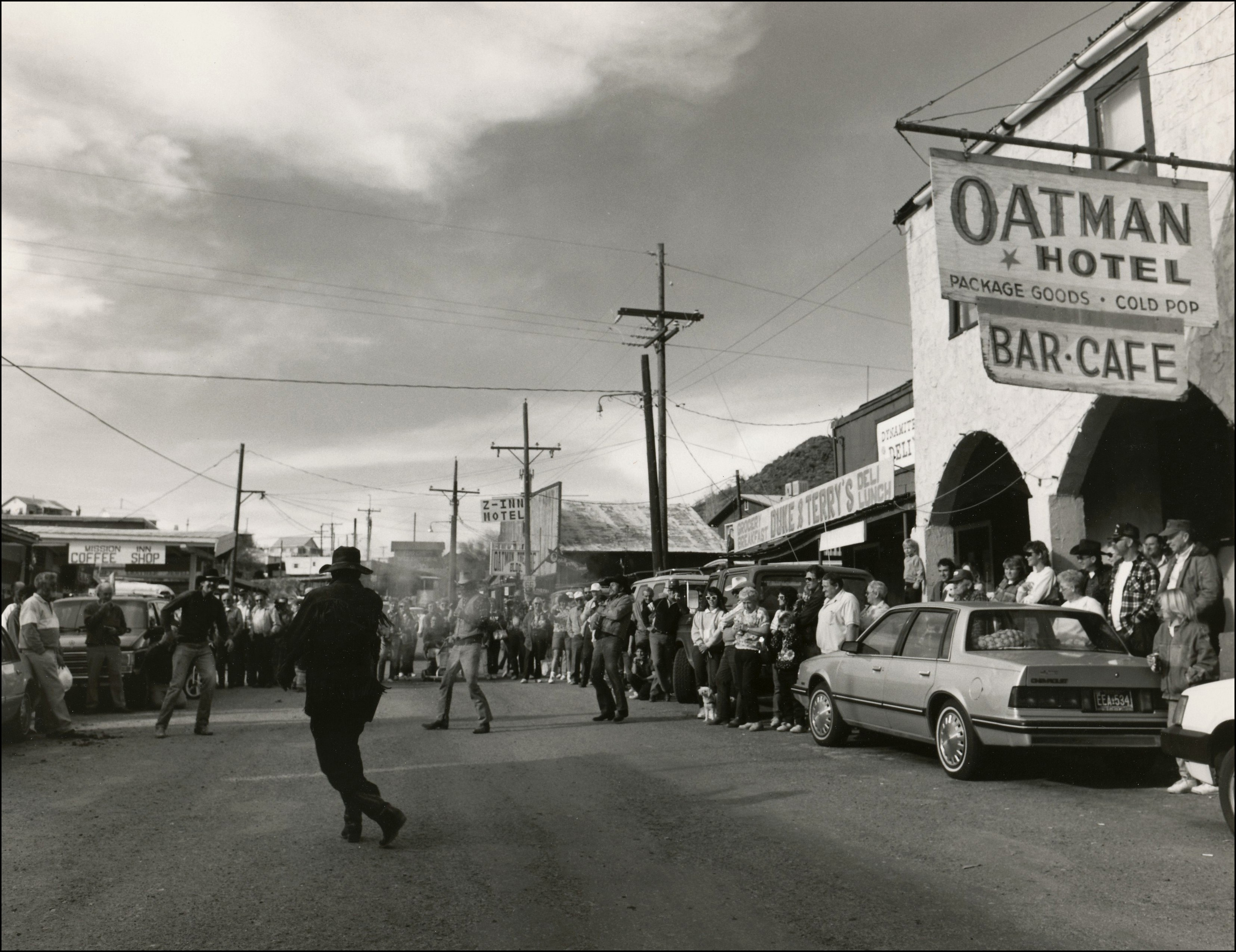 gun fight show in a street with people lined up watching.