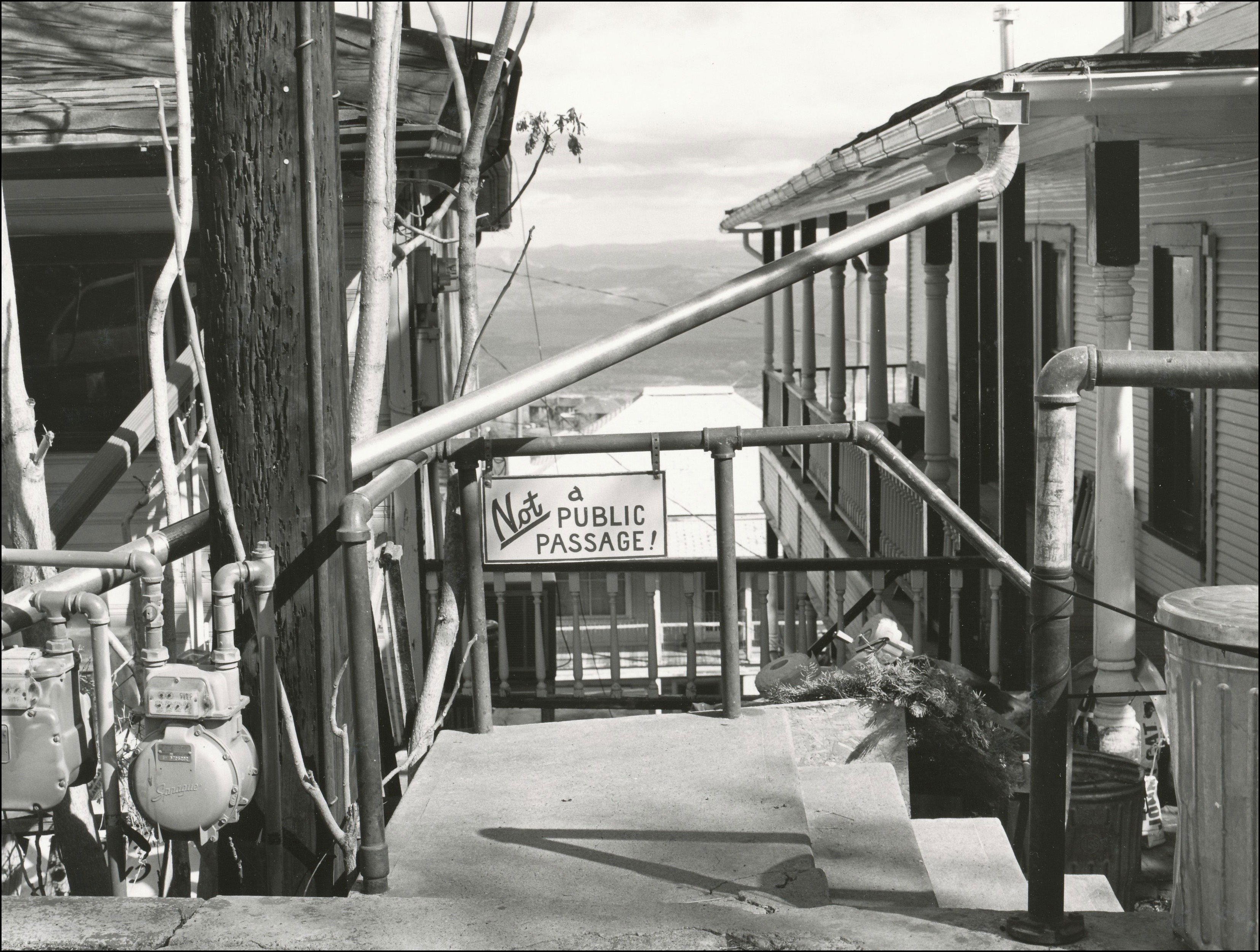 lookng at the back side of old buildings with meter and pipes. sign hanging that says not a public passage