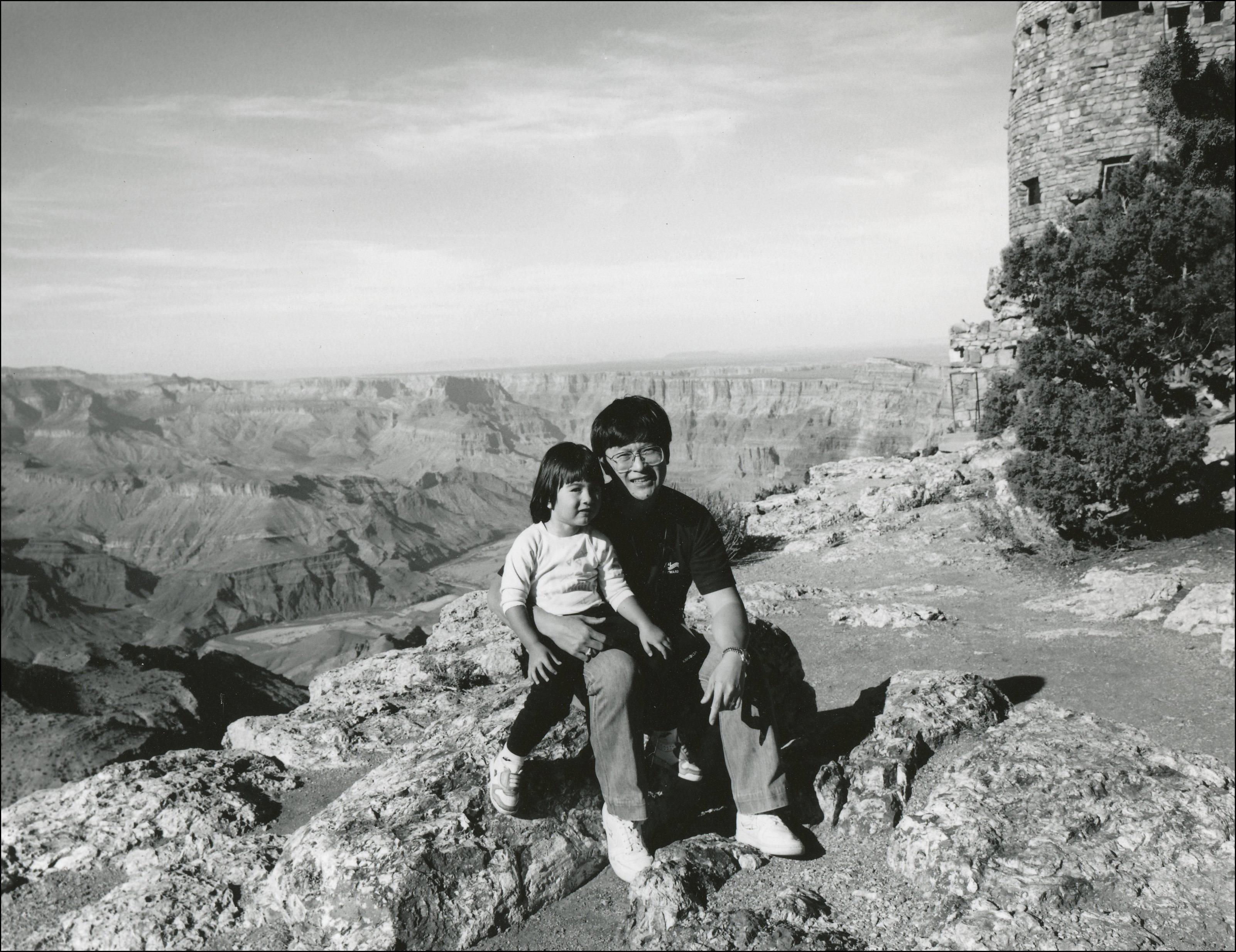 A father and his youg daugher sitting on a rock in front of the Grand Canyon