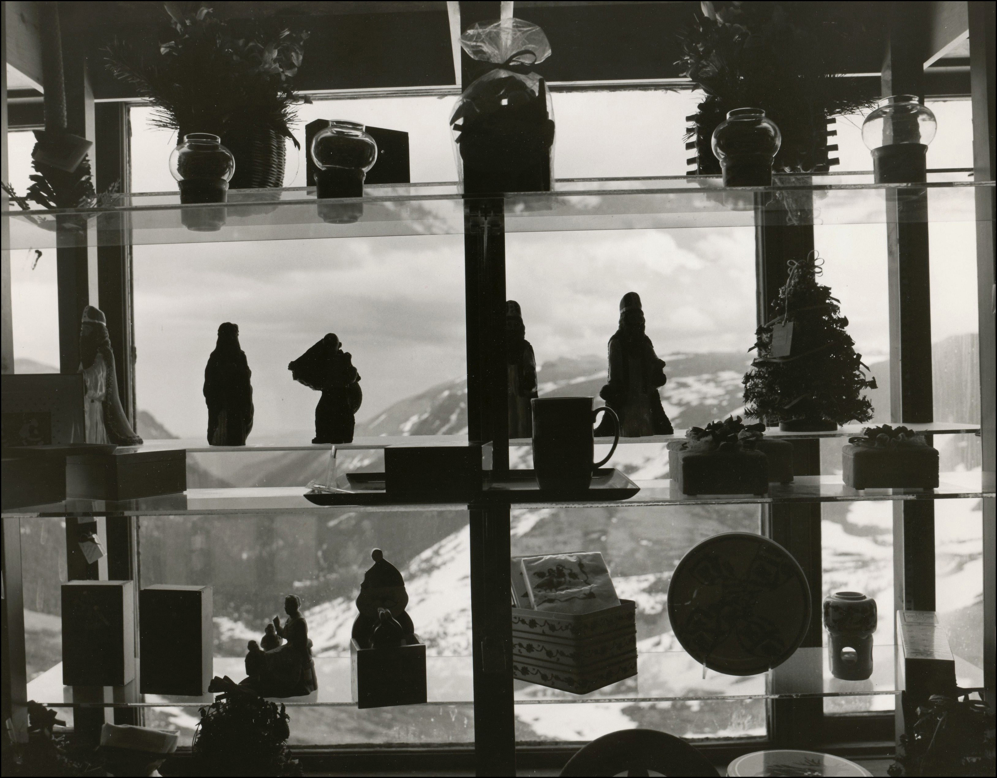 View of shelves in a store with decorative items for sale. Behind the shelves are windows. Mountains covered with snow can be seen through the windows.