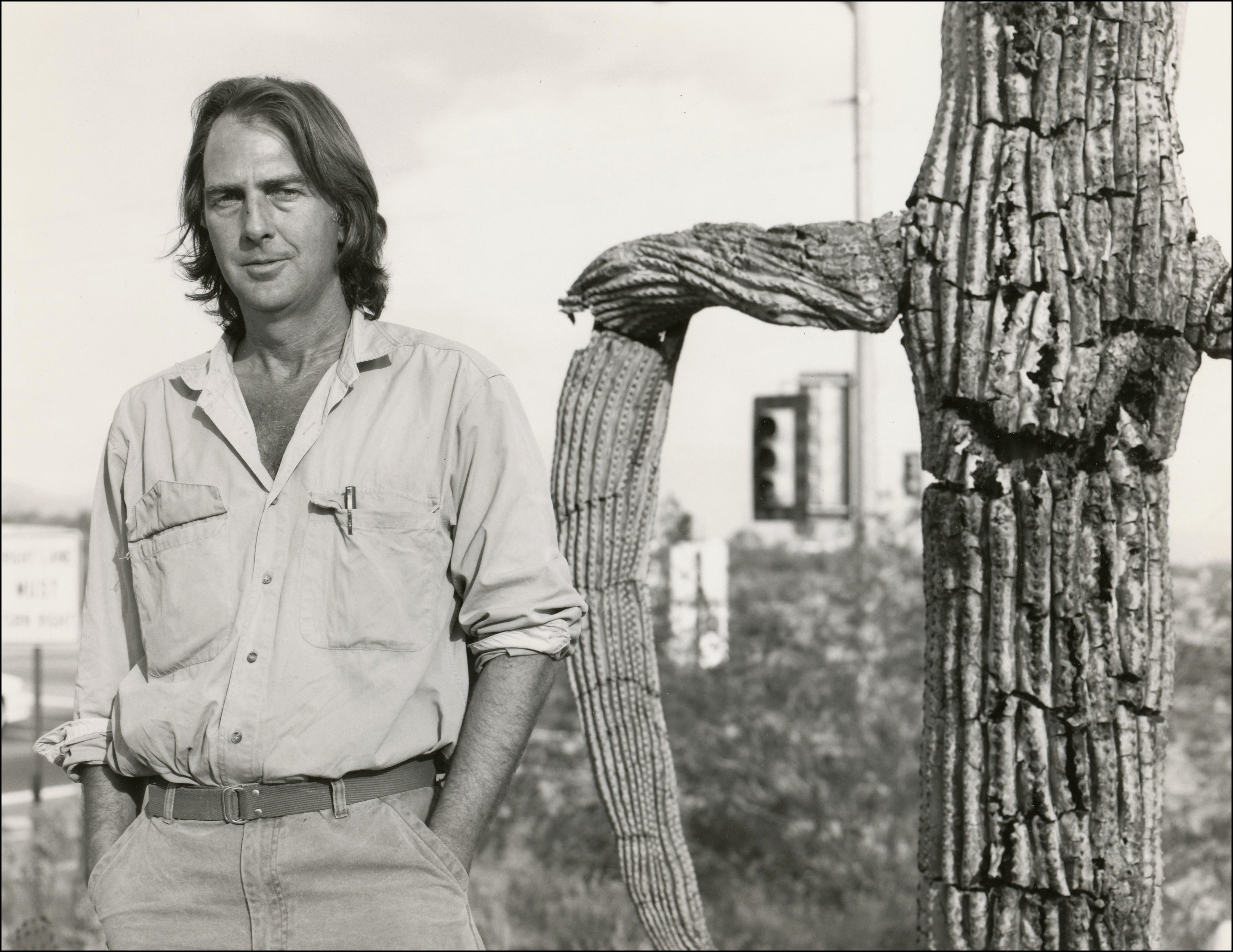 man standing next to old saguaro cactus. Stop light blurred in back ground.