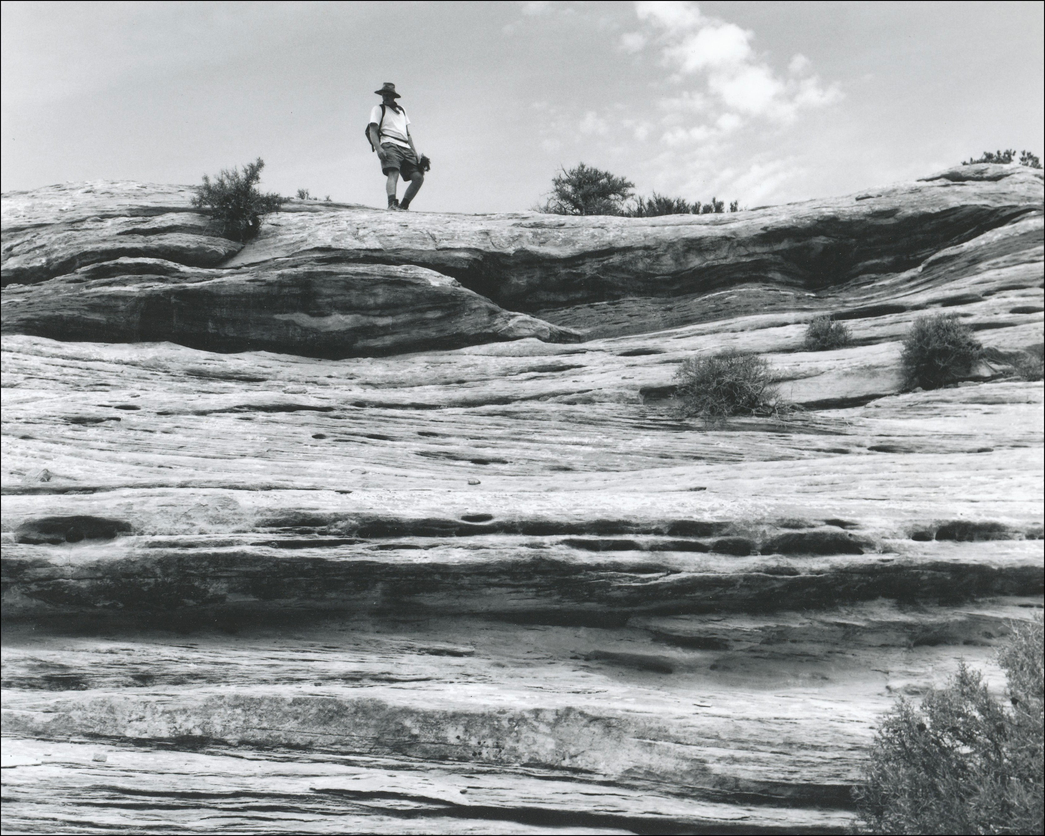 Looking up a rock mountain at man standing on top