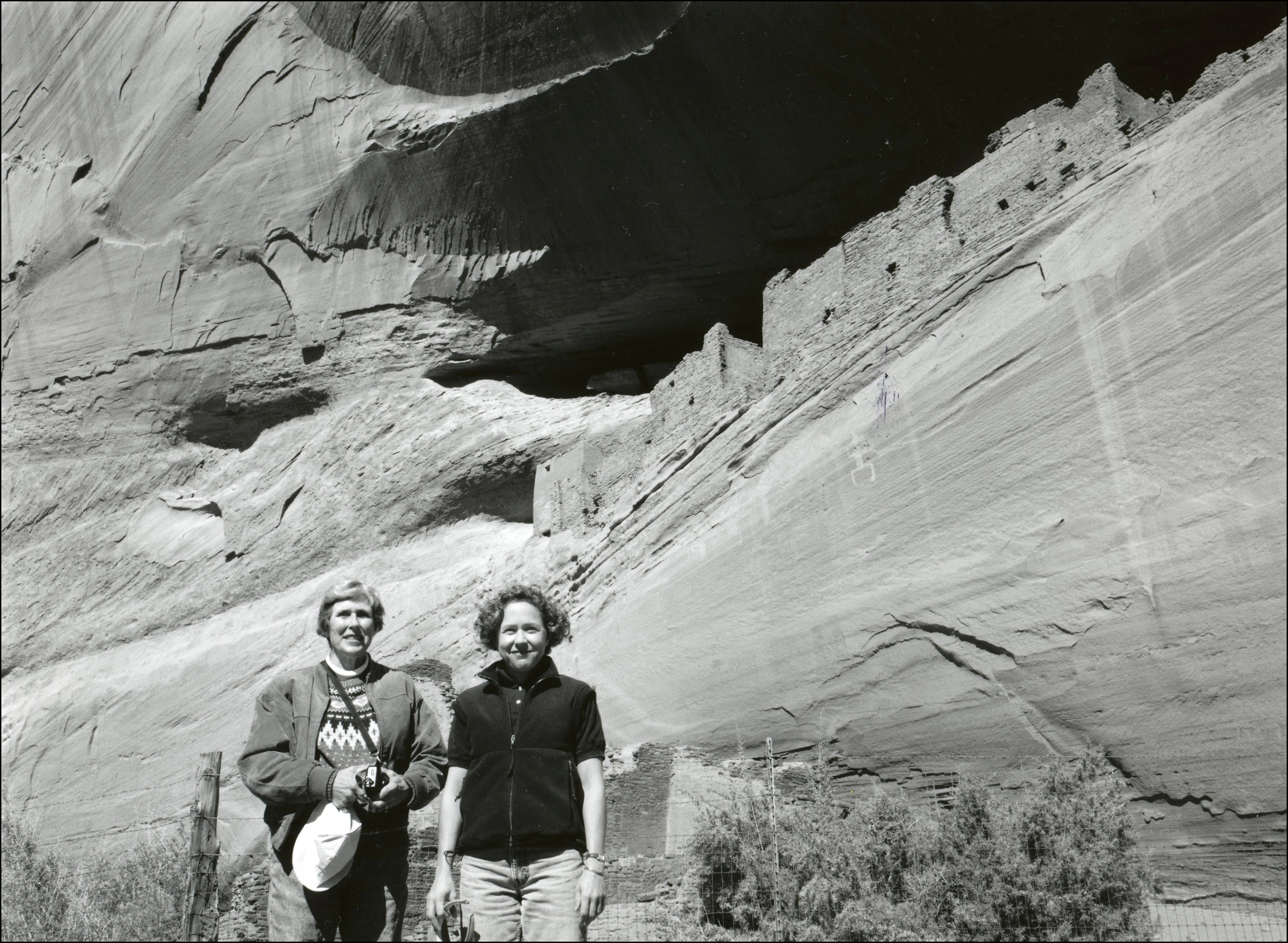 Two women standing in front of old ruins up in large cliff face