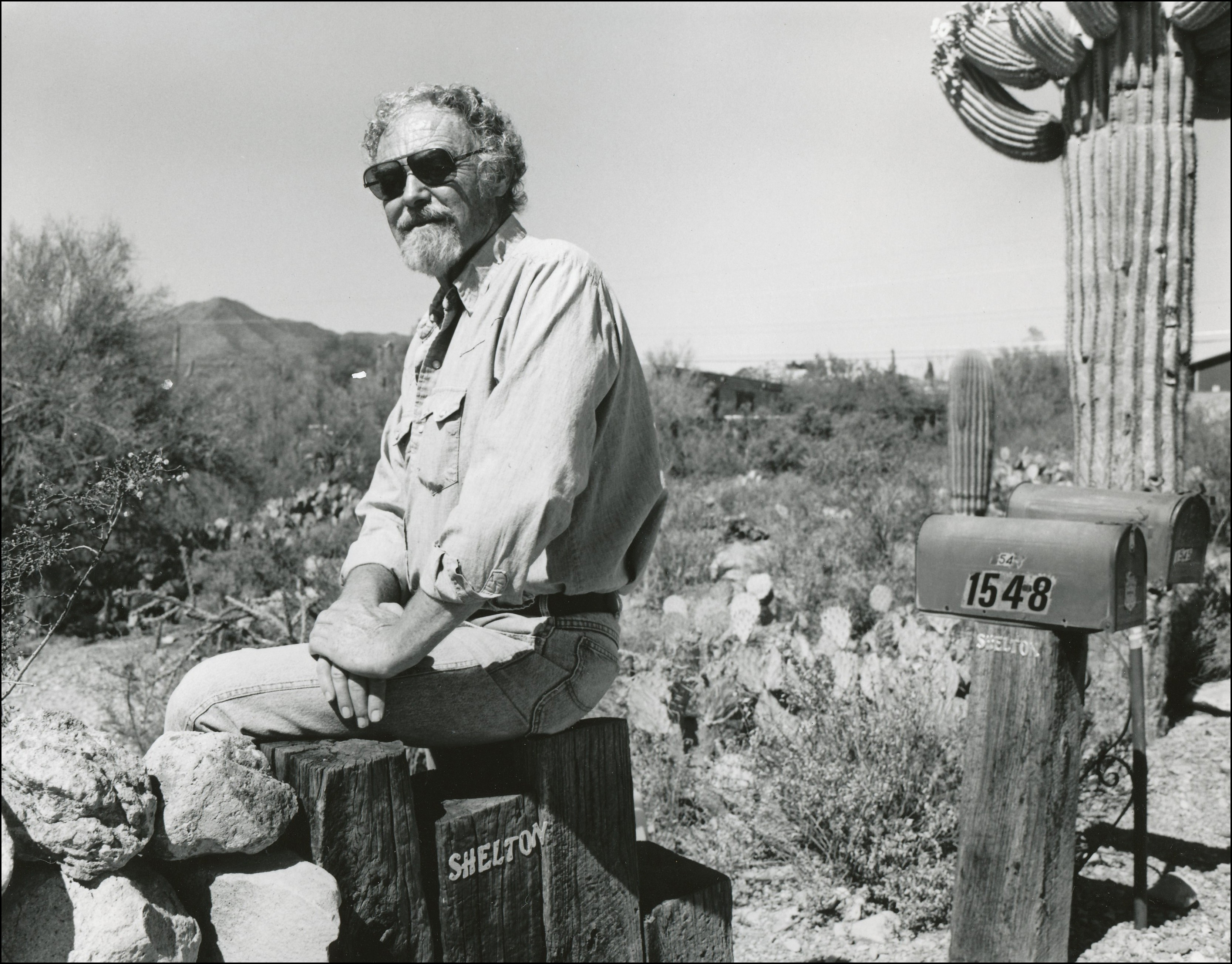 man sitting on the end of a fence next to his mailbox