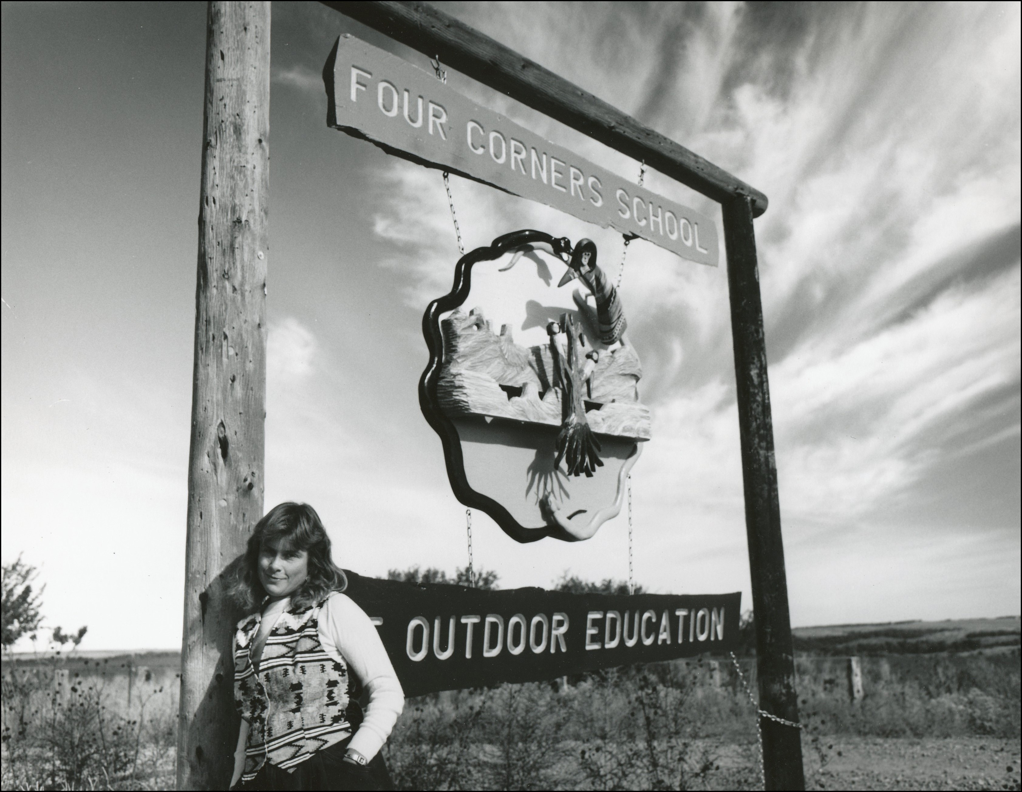 woman leaning against sign post which says "Four Corners School and Outdoor Education"