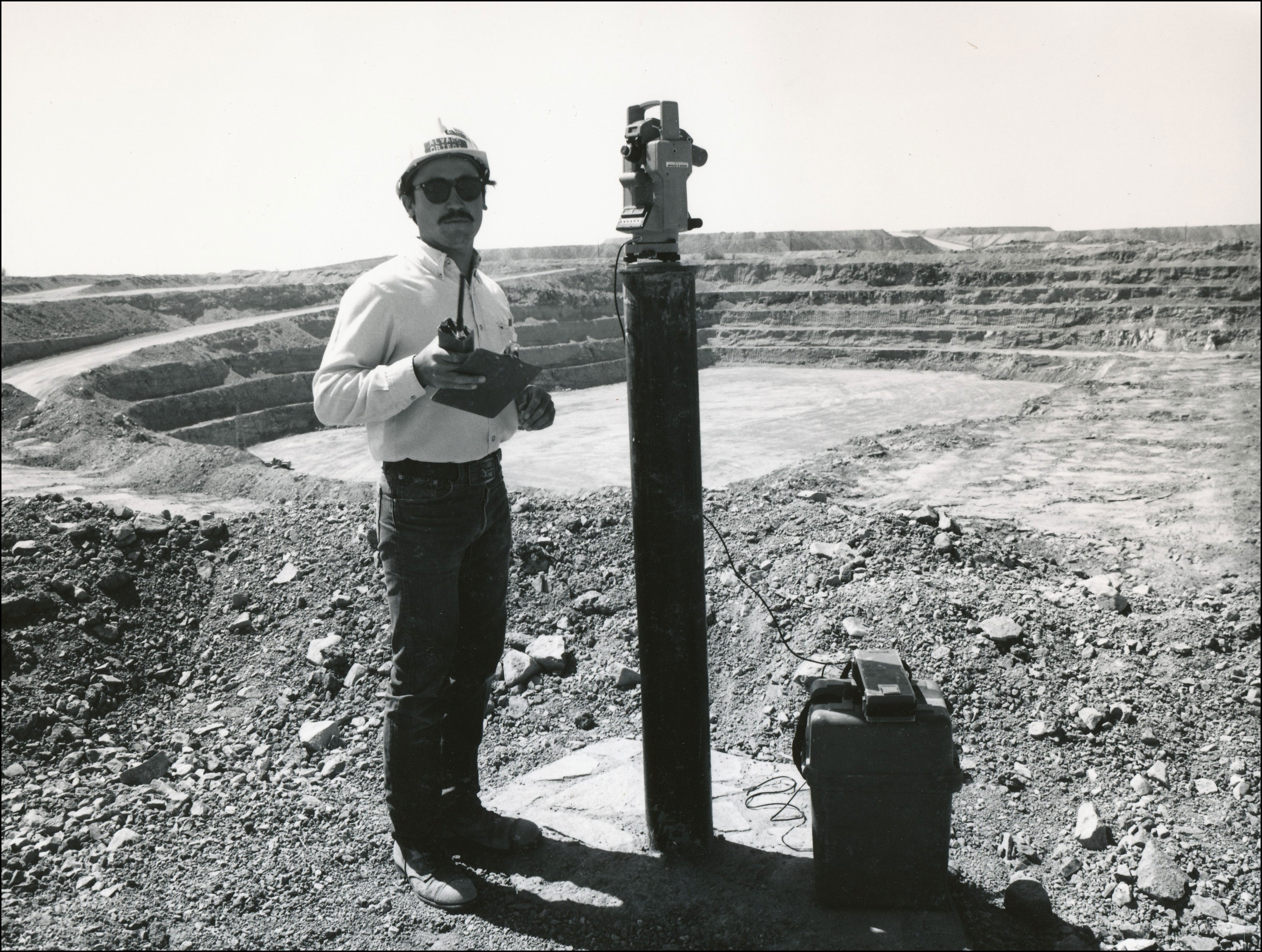 Man in glasses and hard hat standing next to an open mining area