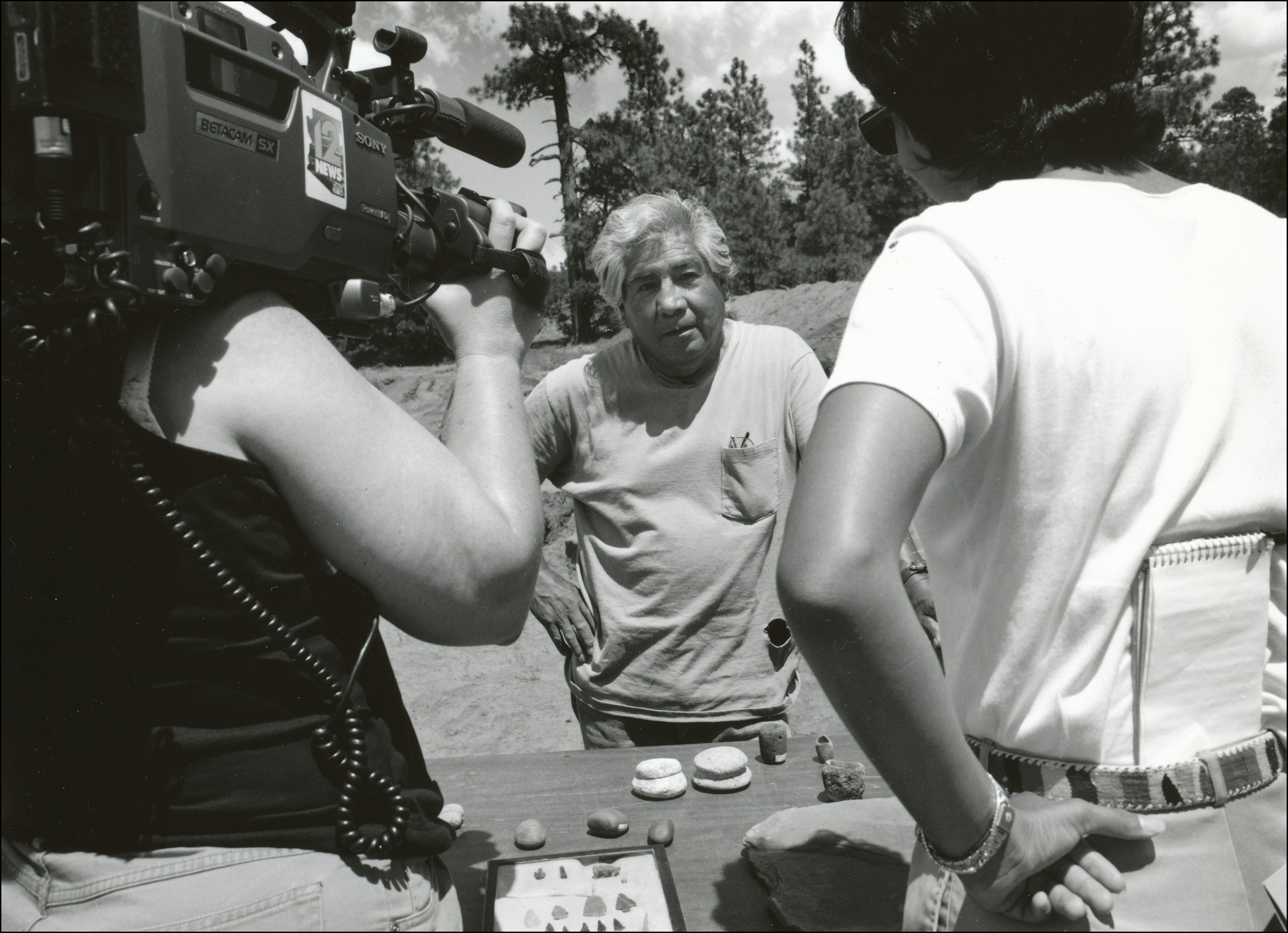 Members of the media with camera speaking with man about archaelogical finds which are layed out on a table