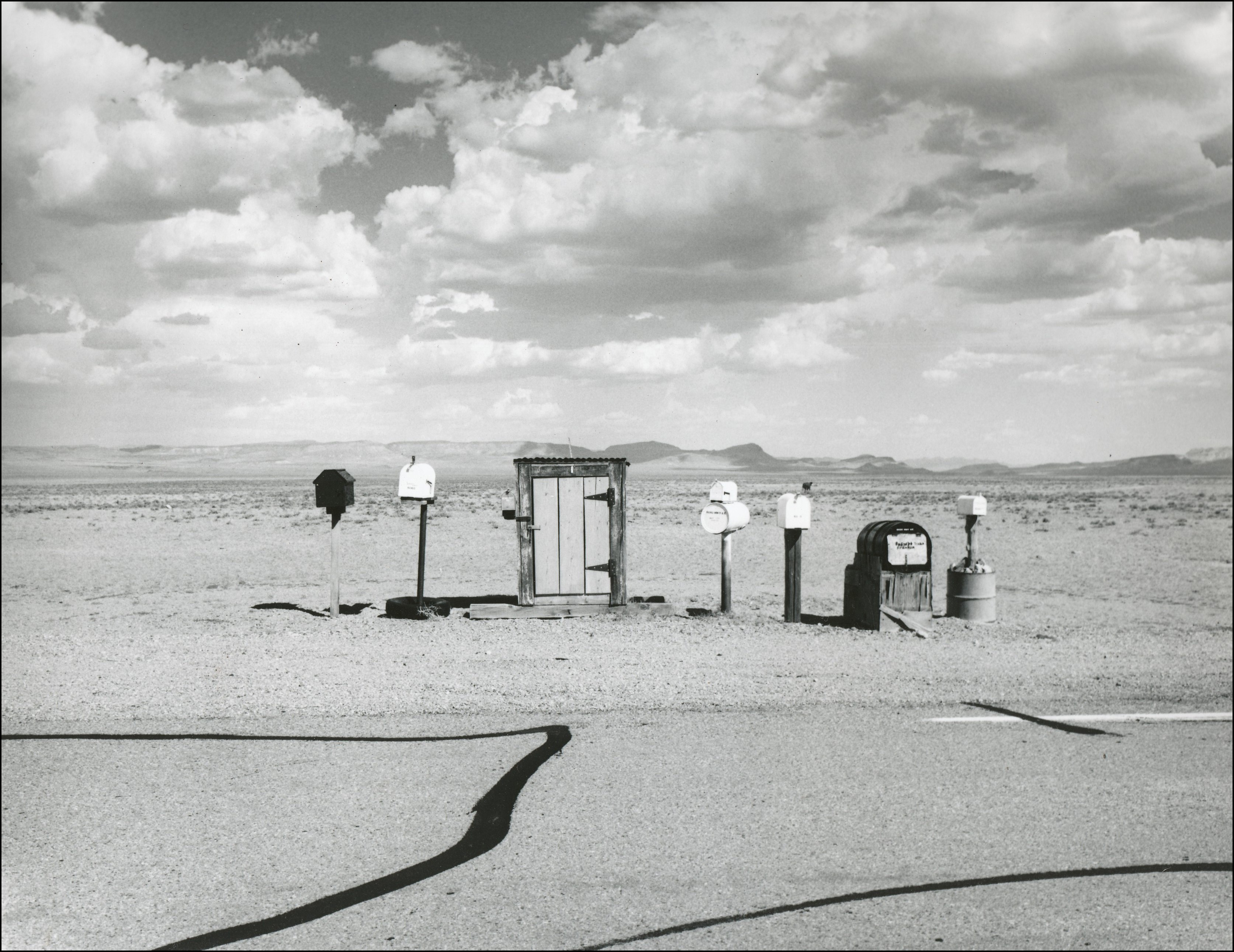 6 mailboxes next to a highway with large spand of land behind and nothing else in site.